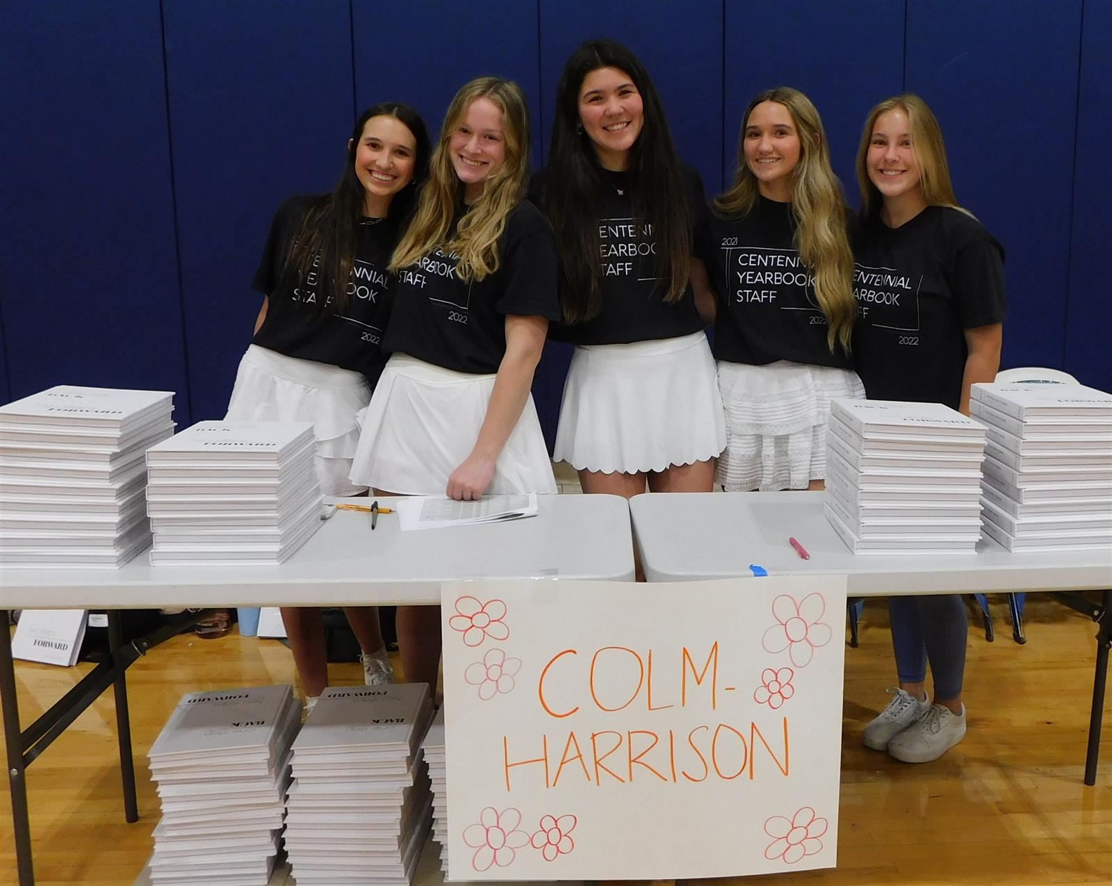 Five females of the yearbook staff behind a table of yearbooks